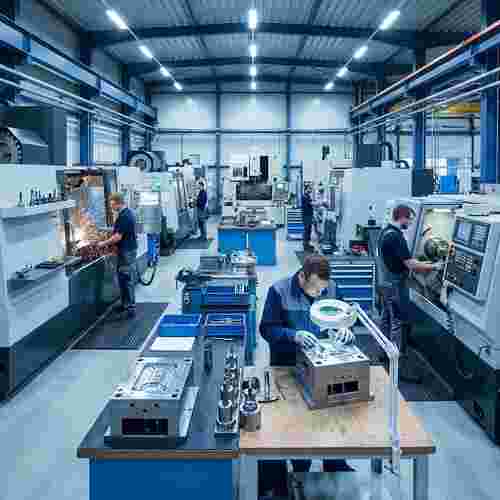 Moderne Spritzgießwerkstatt mit CNC-Fräsen, Drehen und Funkenerosion; Techniker prüfen Teile.