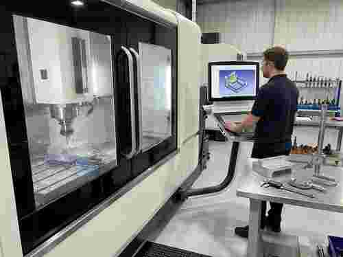 Moderne Werkstatt: CNC-Fräse fräst Aluminiumteil; Techniker prüft CAD/CAM-Modell am Monitor