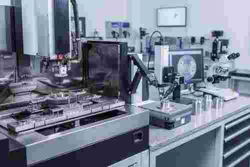 Draht-EDM-Maschine schneidet Metallbauteil; Messstation mit taktilen und optischen Sensoren.