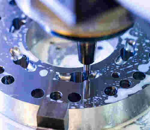 Ein Fräsvorgang bei WT Schmitz an einem runden Metall, in das Löcher gefräst werden. Auf dem Metallgegenstand sindt Flüssigkeitsreste zu sehen vom Fräsvorgang.