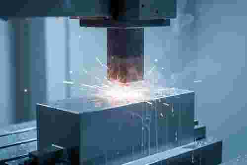 EDM-Maschine im modernen Fertigungsraum, Funkenflug und Kühlnebel über einem gehärteten Stahlwerkstück.