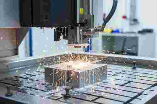 Nahaufnahme eines Draht-EDM-Prozesses in moderner Fertigung mit orange Funken und Kühlmittel.