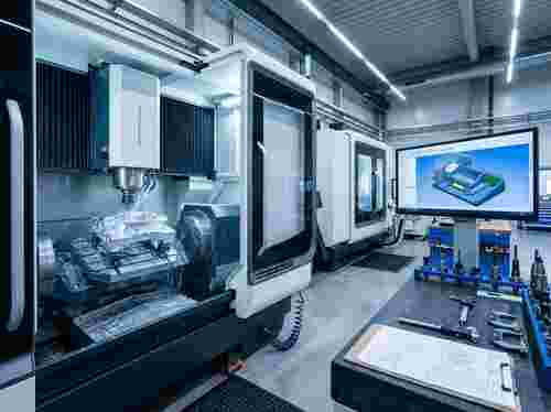 Moderne CNC-Werkstatt mit Fünf-Achs-Fräse beim Metallbearbeiten; CAD/CAM-Arbeitsplatz
