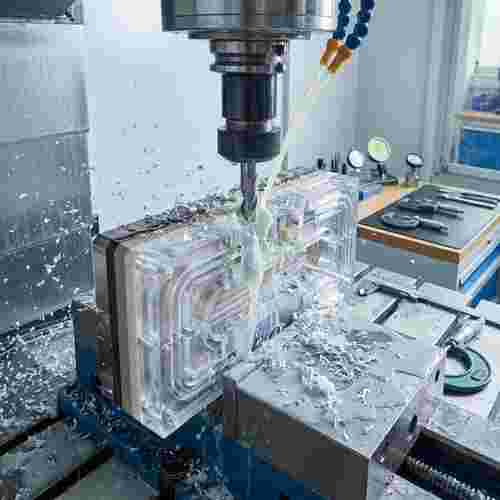 CNC-Fräsmaschine bearbeitet komplexes Kunststoffteil mit Kanälen; Späne und Kühlmittel sichtbar.
