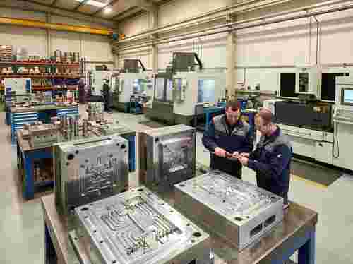 Moderne Spritzgießwerkstatt mit Stahl- und Aluminiumsformen; Techniker prüft Formhälften.