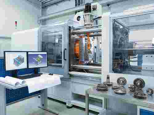 Spritzgießanlage injiziert Kunststoff in Präzisionsform; CAD-Pläne auf dem Schreibtisch.