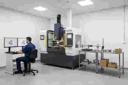 Fotorealistisches Quadratbild einer modernen Draht-EDM-Werkstatt: EDM-Maschine, Monitor, Prüfung.