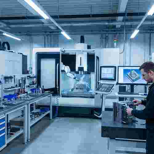 Spritzgießwerkstatt: CNC-Fräse formt Stahlwerkzeug; Techniker prüft Messschieber.